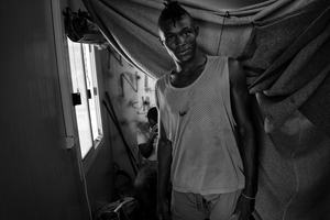 Ali, a professional football player from Guinee, inside his container at the refugee camp Moria. He lives together with 4 other refugees from Africa, their beds divided by blankets.